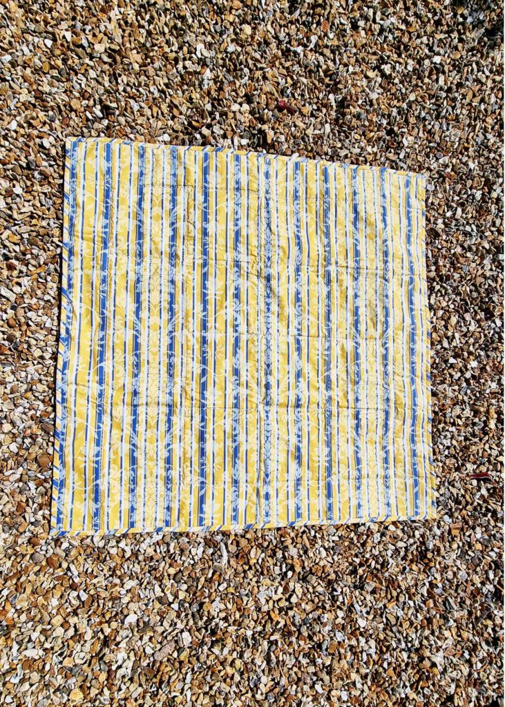 Back of picnic blanket showing stripy yellow white and blue curtain fabric